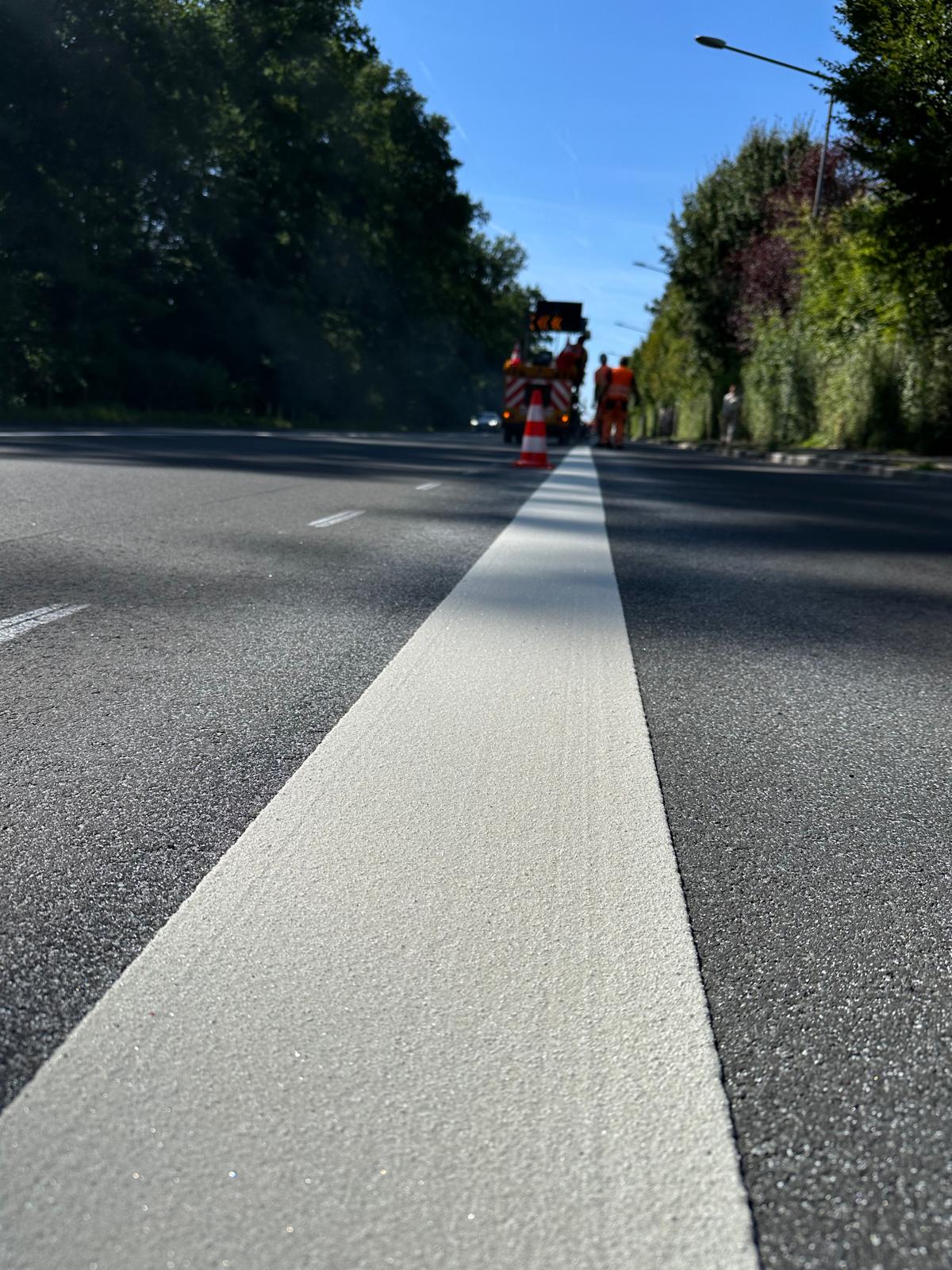 Frisch aufgebrachte weiße Längslinie auf der Fahrbahn – SP-Team mit Absicherung im Hintergrund