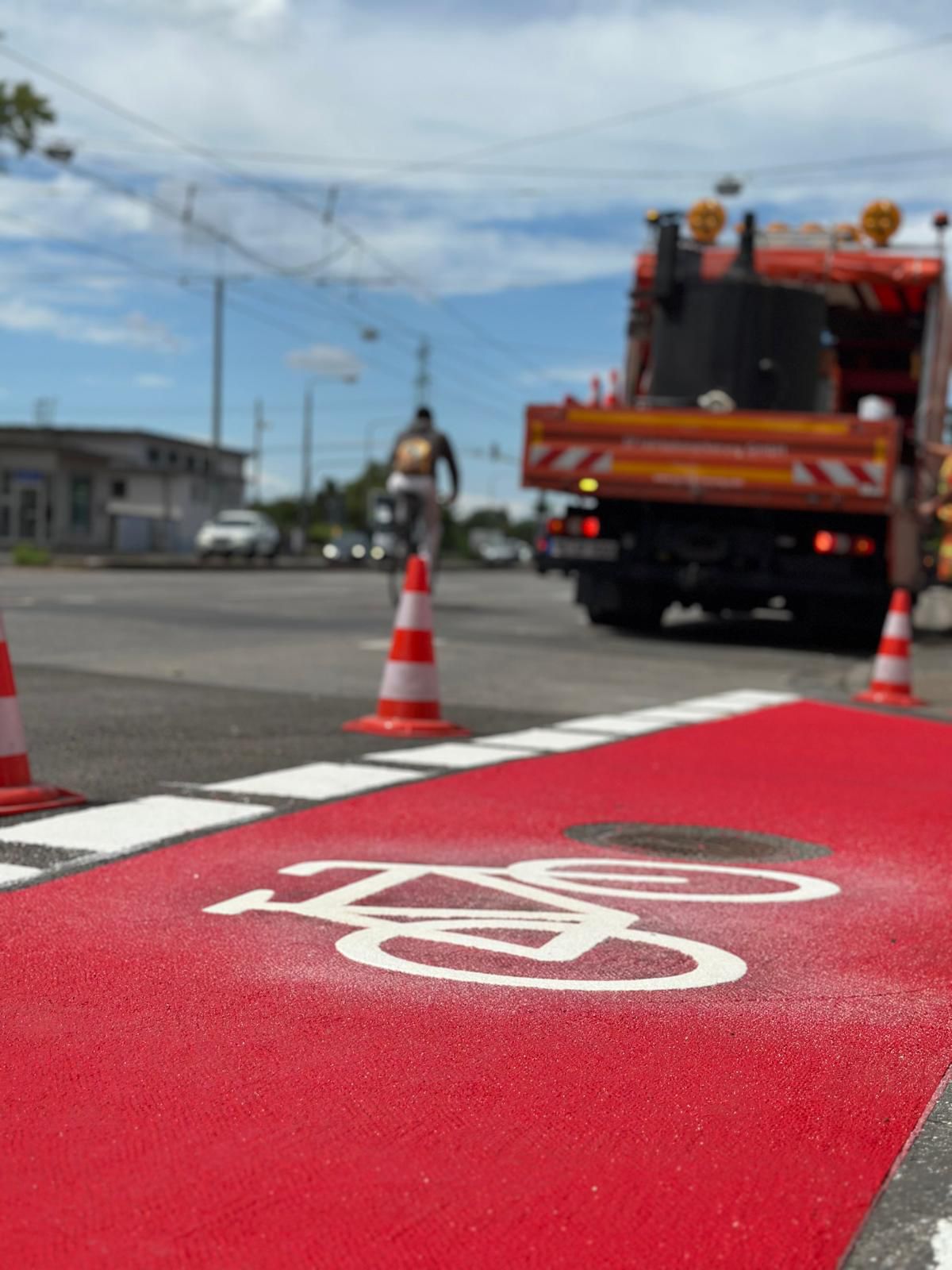 Fertiger roter Radweg mit weißem Fahrrad-Piktogramm – SP-Markierungsfahrzeug im Hintergrund