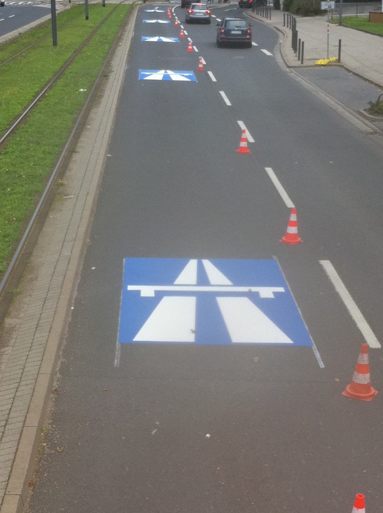 Verkehrssymbole auf Stadtstraße – blaue Autobahnzeichen als Bodenmarkierungen