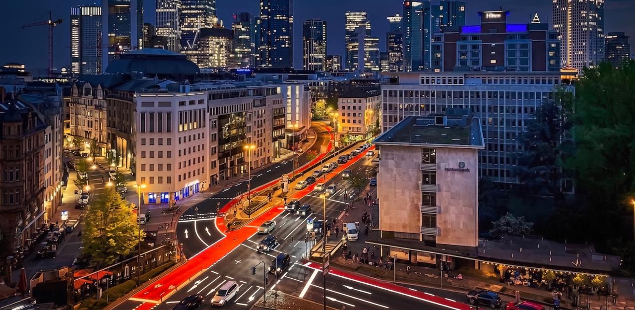 Frankfurter Skyline mit beleuchteten Straßen und leuchtenden Fahrbahnmarkierungen bei Nacht